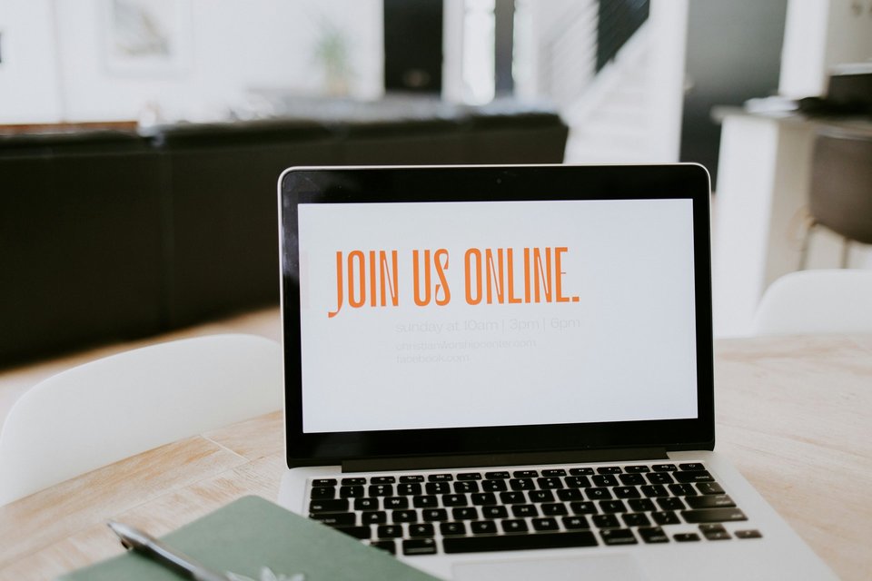 Ein aufgeklappter Laptop, der auf einem Schreibtisch steht. Der Bildschirm ist weiß. In orange steht auf dem Bildschirm Join us online.