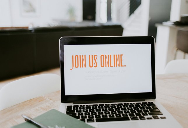 Ein aufgeklappter Laptop, der auf einem Schreibtisch steht. Der Bildschirm ist weiß. In orange steht auf dem Bildschirm Join us online.